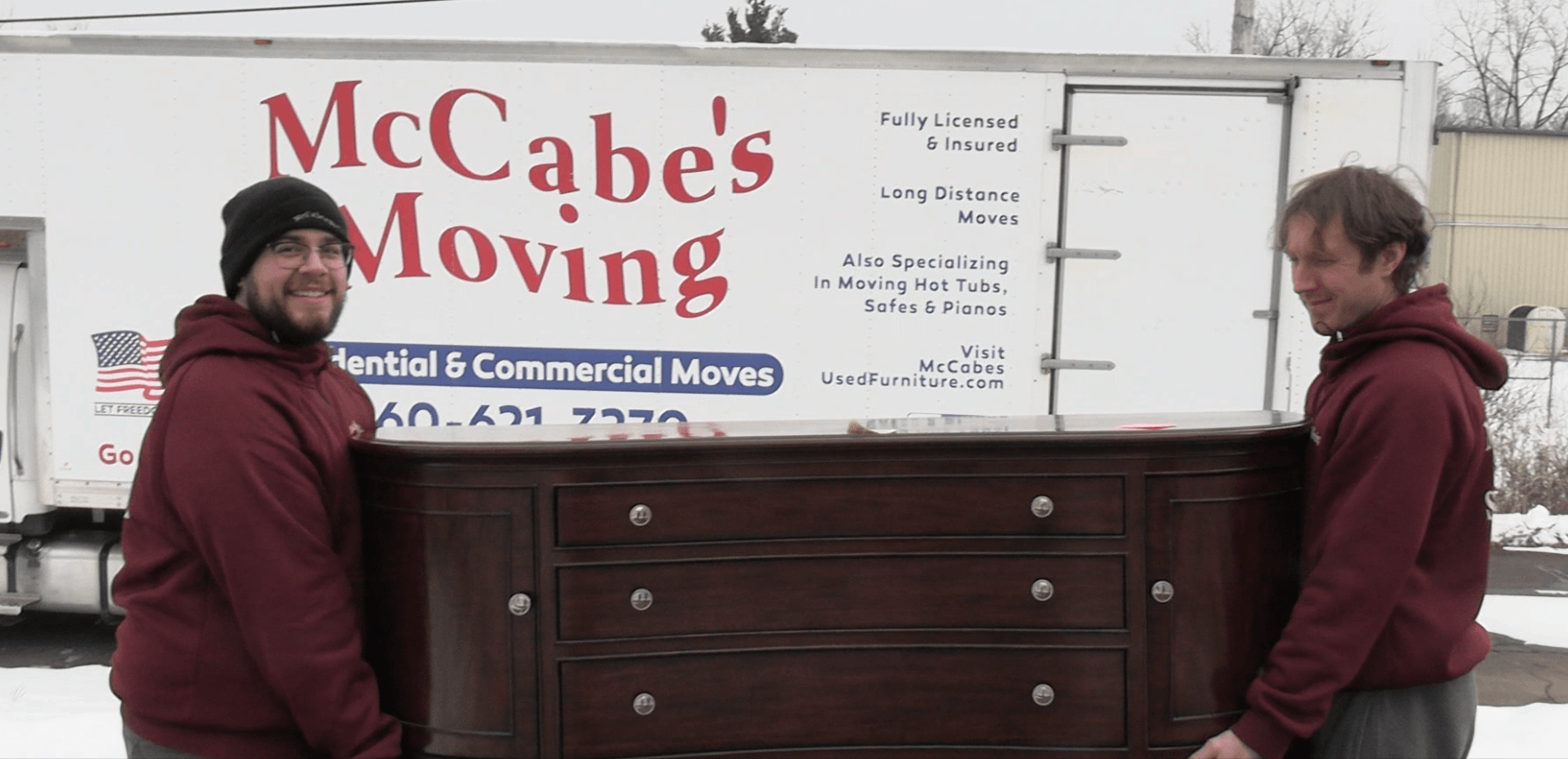 Two McCabe's Moving crew members carrying a dresser in front of the company truck